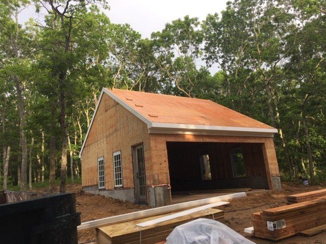 Construction of a garage building with a sloped roof in a wooded area. Unfinished wood exterior and roof.