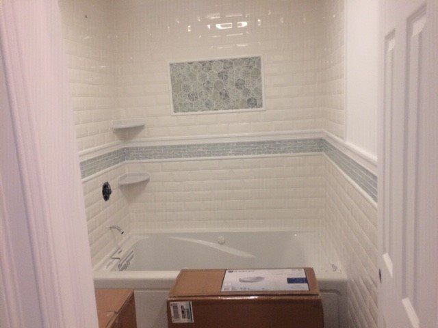 Bathroom with white tile, bathtub, accent tile strip, and door.