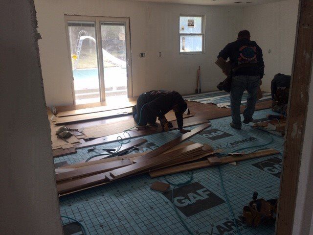 Men installing hardwood flooring in a room with a sliding door to a pool.
