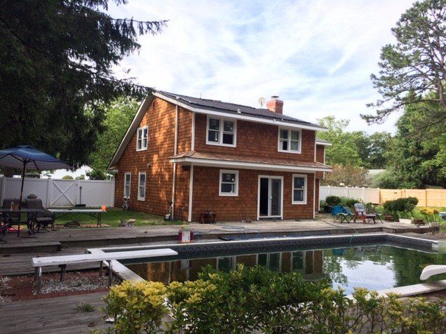 Two-story house with cedar siding, windows, and chimney, overlooking a backyard pool.