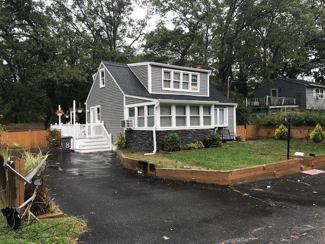Gray house with white trim, porch, and a dormer, with asphalt driveway, and wooden fence.