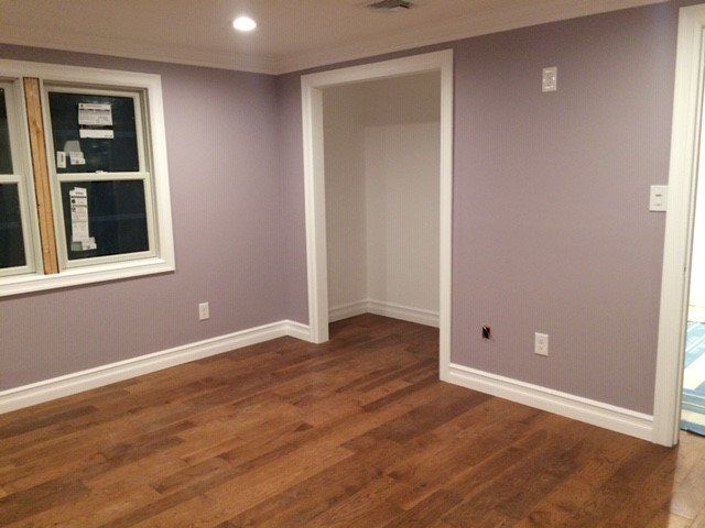 Empty room with wood floors, lavender walls, white trim, and a window.