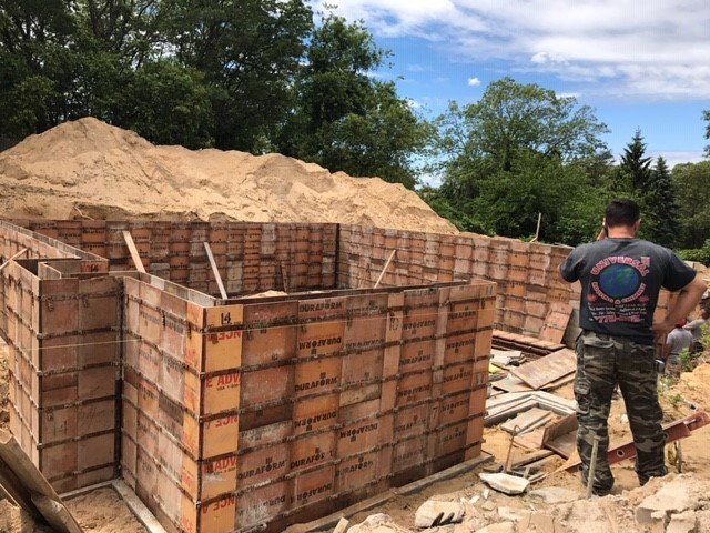 Construction site with wooden forms for a concrete foundation; a worker stands nearby.