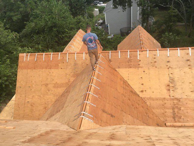 Construction worker walking on a plywood roof, attaching metal clips. Outdoor setting.