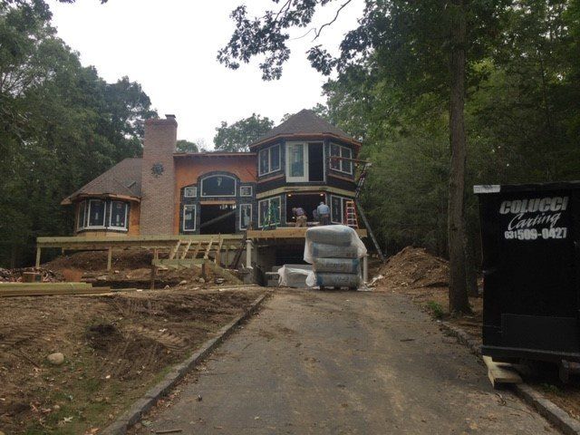 House under construction with driveway. Brick chimney, circular structure, and debris visible.