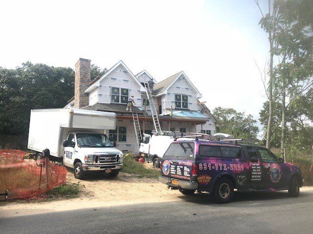 Construction site with trucks, a house under renovation, and workers on ladders.