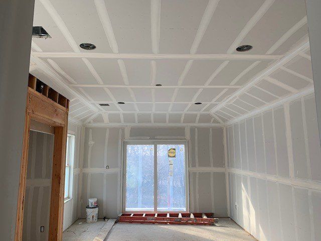 Interior of a room under construction, with drywall on walls and ceiling. Sliding glass doors and recessed lighting.