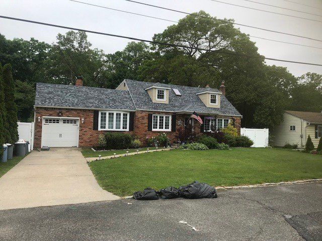 Brick house with a gray shingle roof, green lawn, and white garage door.