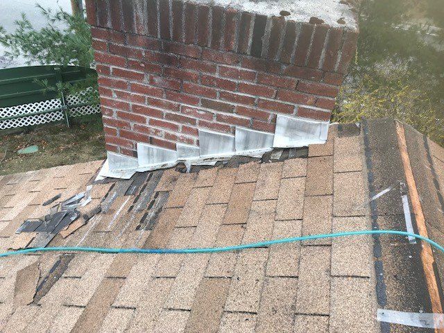 Chimney on a roof with damaged shingles and flashing.