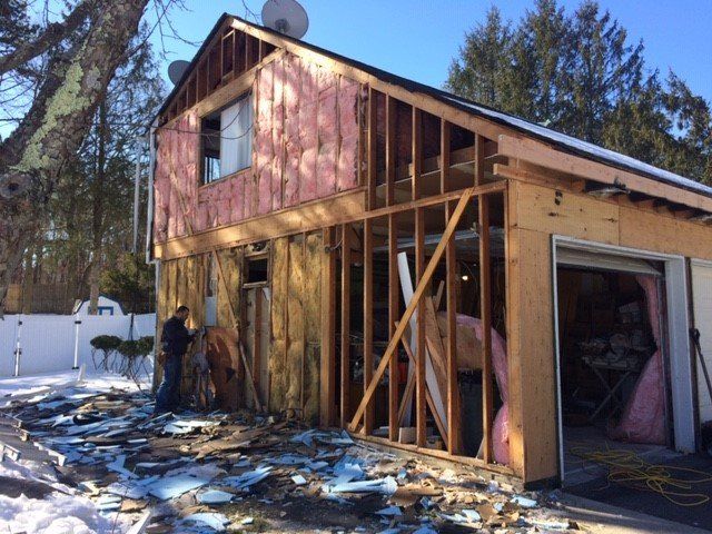 Garage under construction; insulation exposed. Man standing beside the building. Blue sky, snow on the ground.