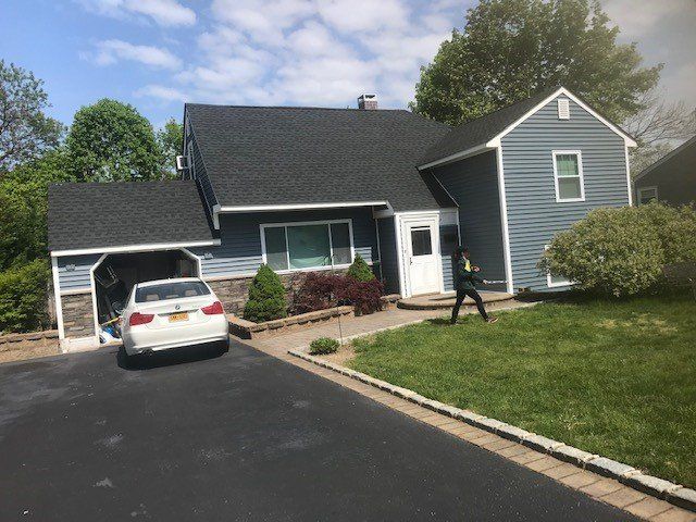 Blue house with a black roof, driveway, and car parked under a carport. Person in yard.