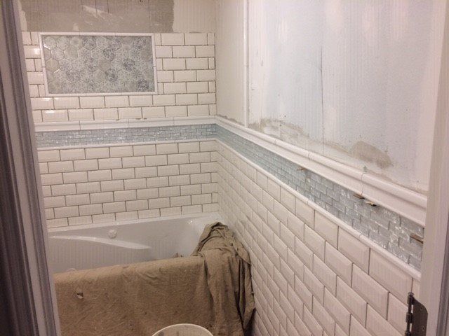 Bathroom with white subway tile, a decorative tile border, and a built-in shelf.