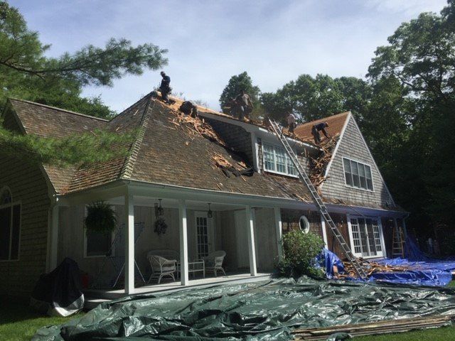 Roof of a house under construction. Workers on the roof, ladder present, tarps on the ground.