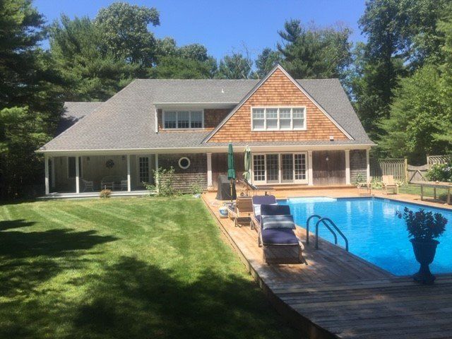 House with pool and deck, surrounded by lawn and trees, sunny day.