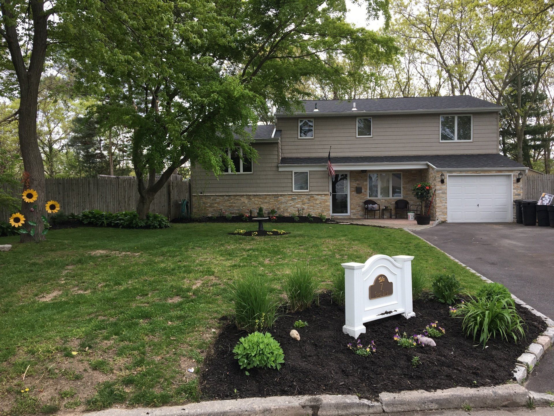 Two-story house with green lawn, stone accents, and a white garage door.  A sign sits in the front yard.