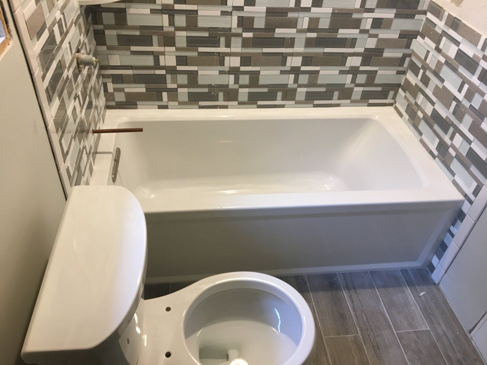 Bathroom with white tub, toilet, and gray tile backsplash.