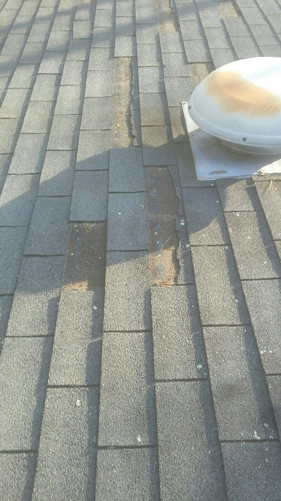Asphalt shingles on a roof with visible water damage and a white ventilation fan.