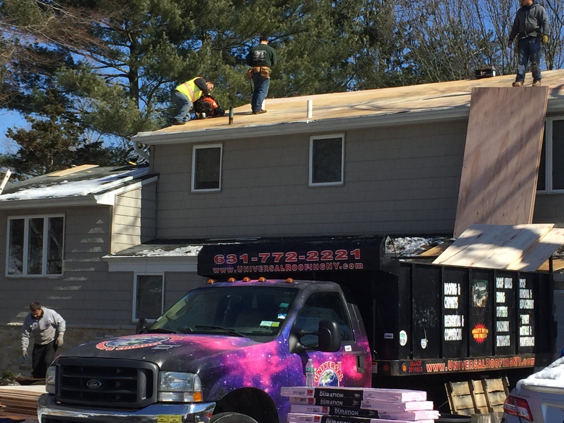 Roofers on a house with a truck featuring galaxy-themed graphics parked in front.