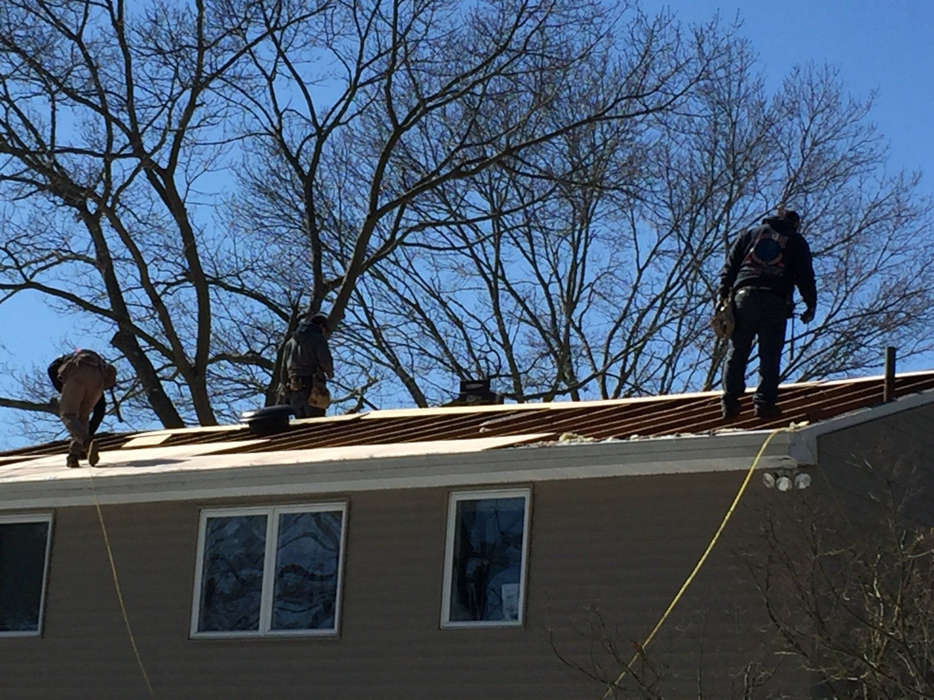 Three workers on a rooftop with safety ropes, clear sky.