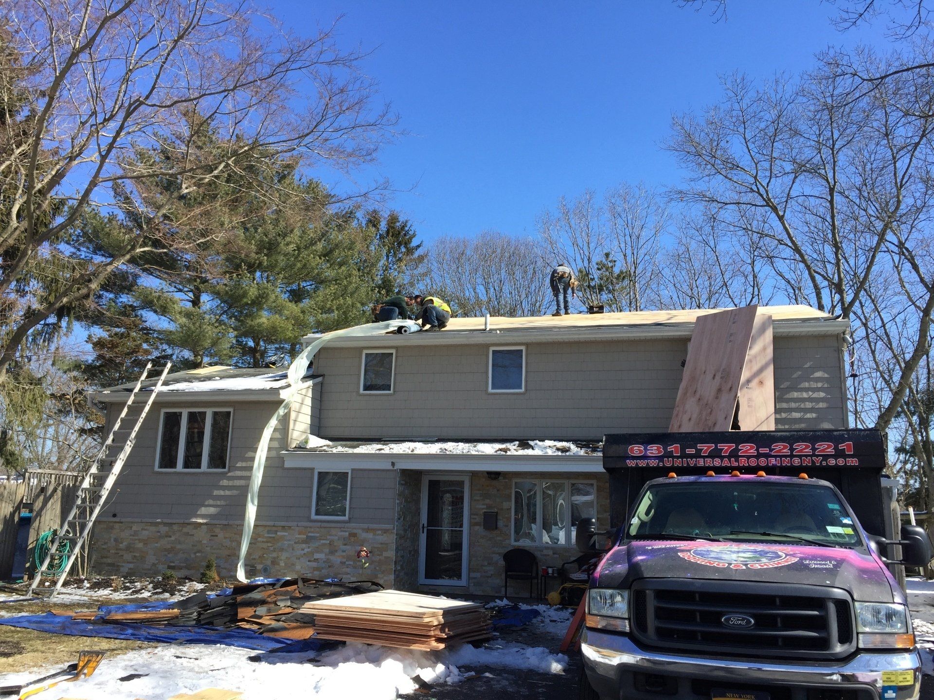Two-story house with roofing work in progress; workers on roof; truck in foreground; clear sky.