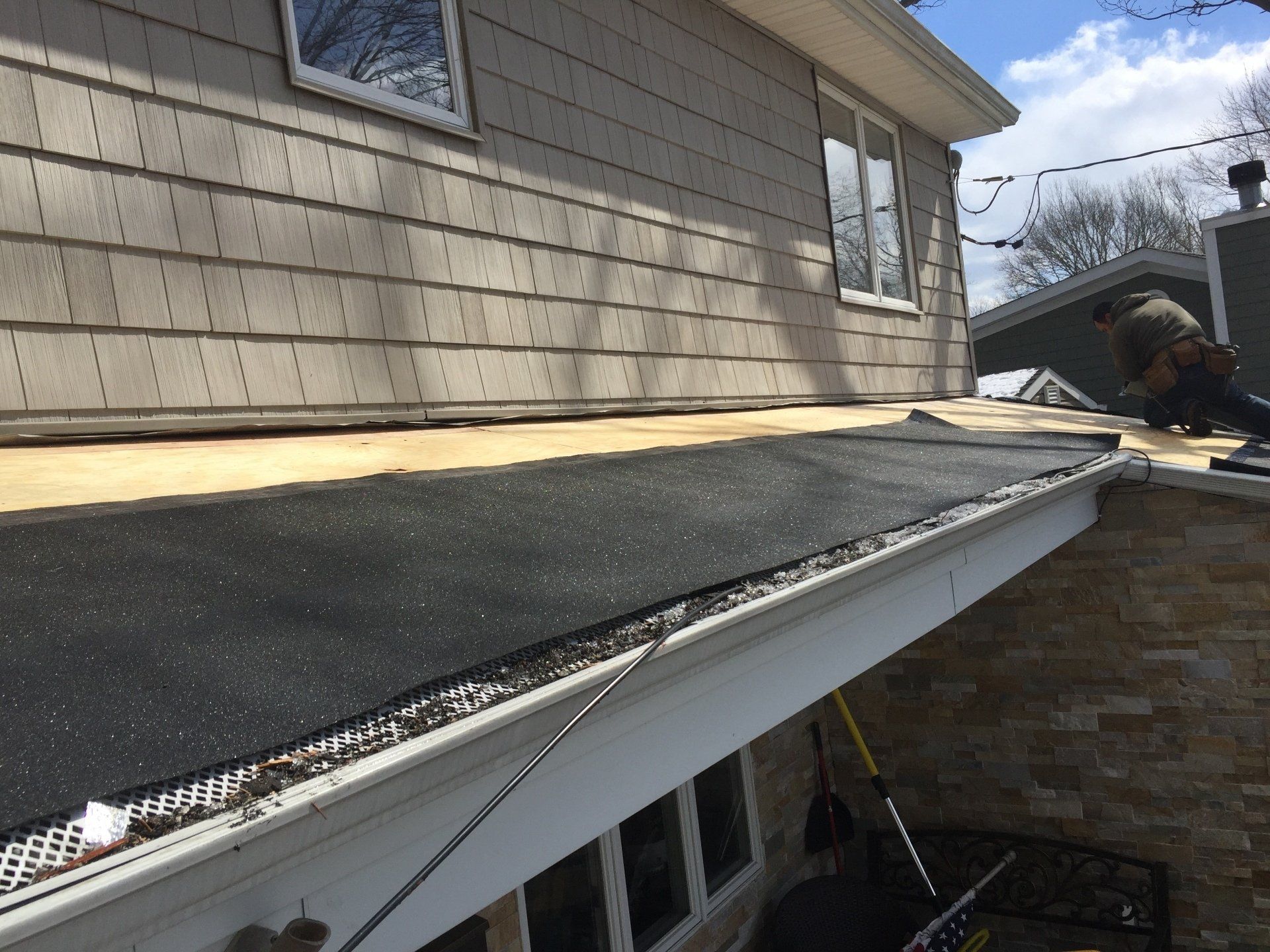 Roof of a house with black material and a worker. Gutters with leaf guards.