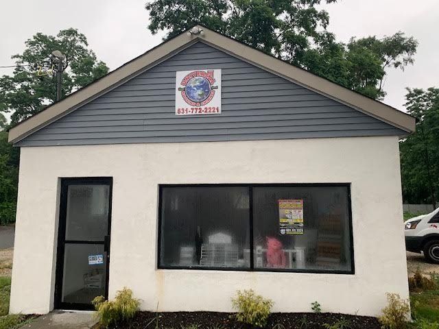 A small building with a sign above the window. Gray siding, white walls, and a black-framed window.