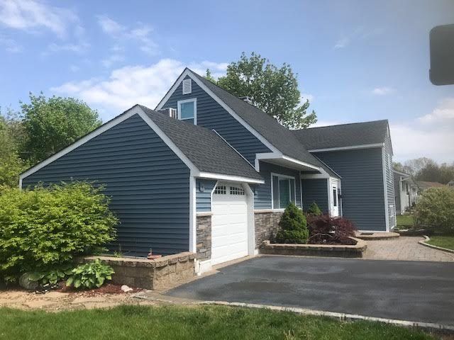 Blue sided house with a black roof, white garage door, and stone accents.