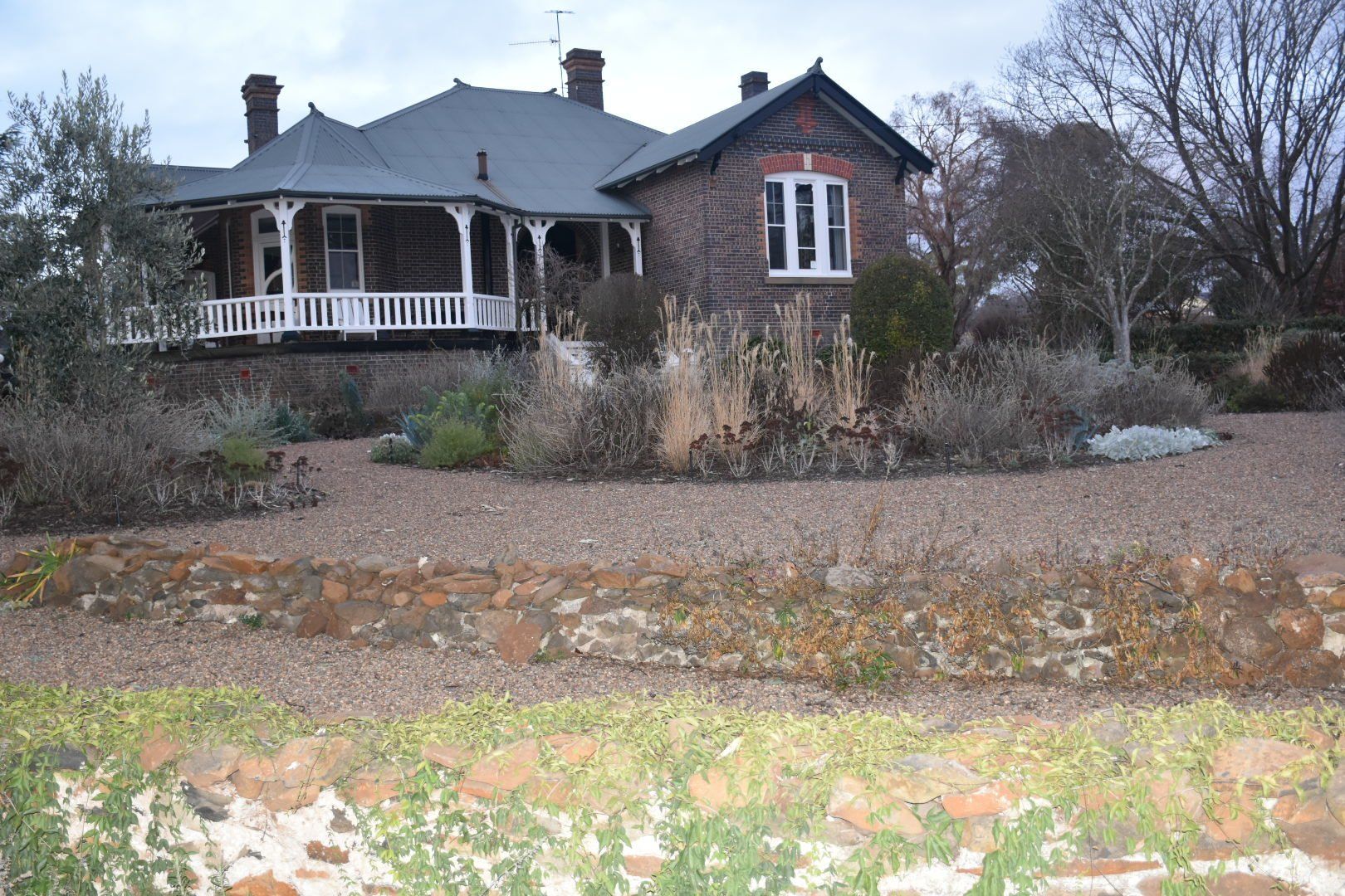a large brick house with a porch is surrounded by gravel and trees