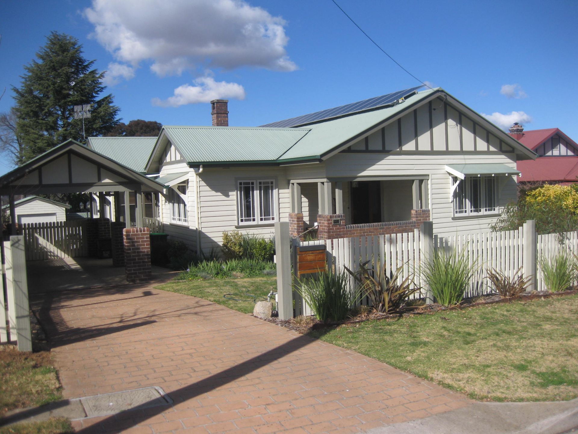 view from the street of a freshly painted heritage style house with a green roof and a white picket fence