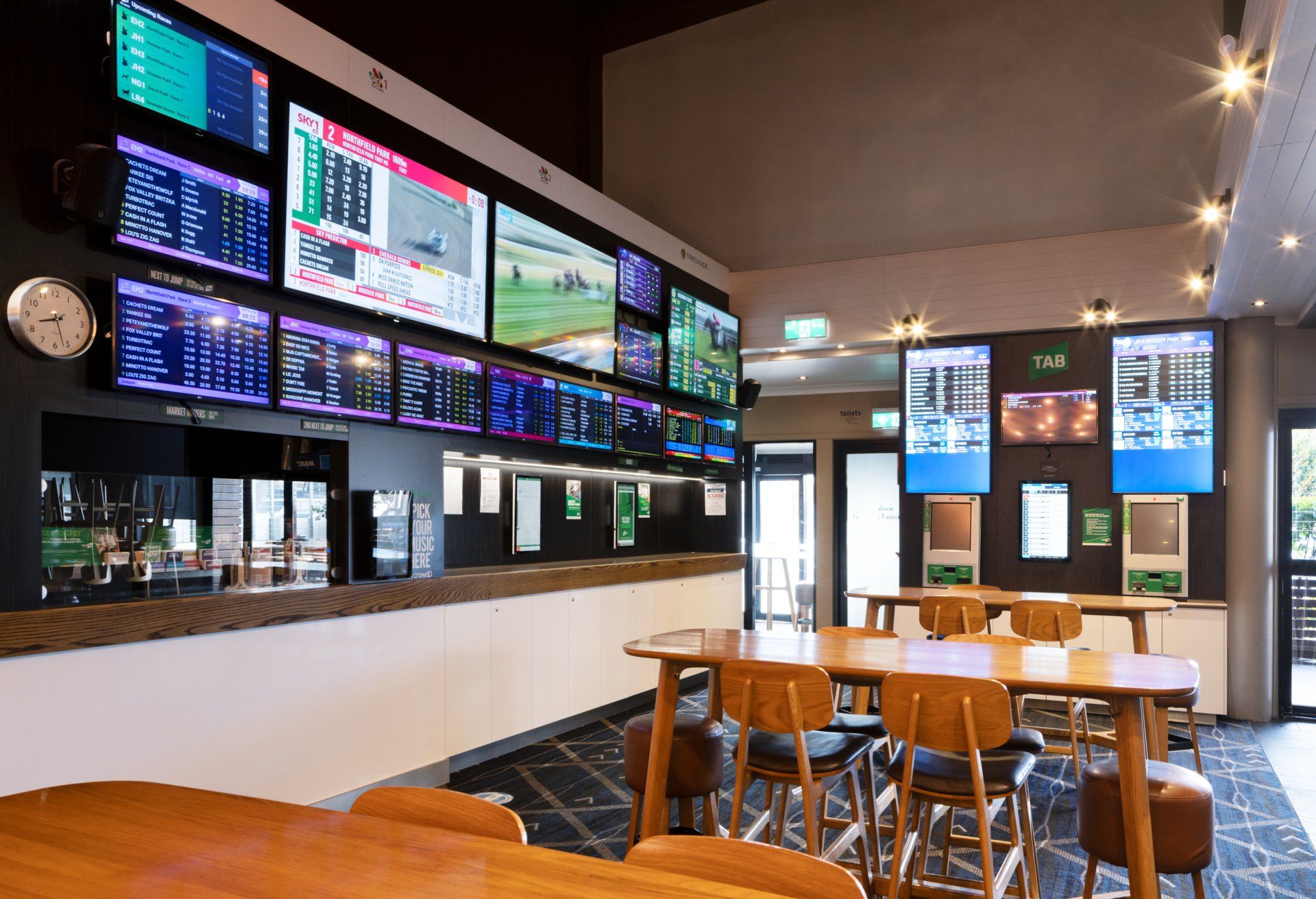 a dining room with tables and chairs and lots of televisions on the wall .