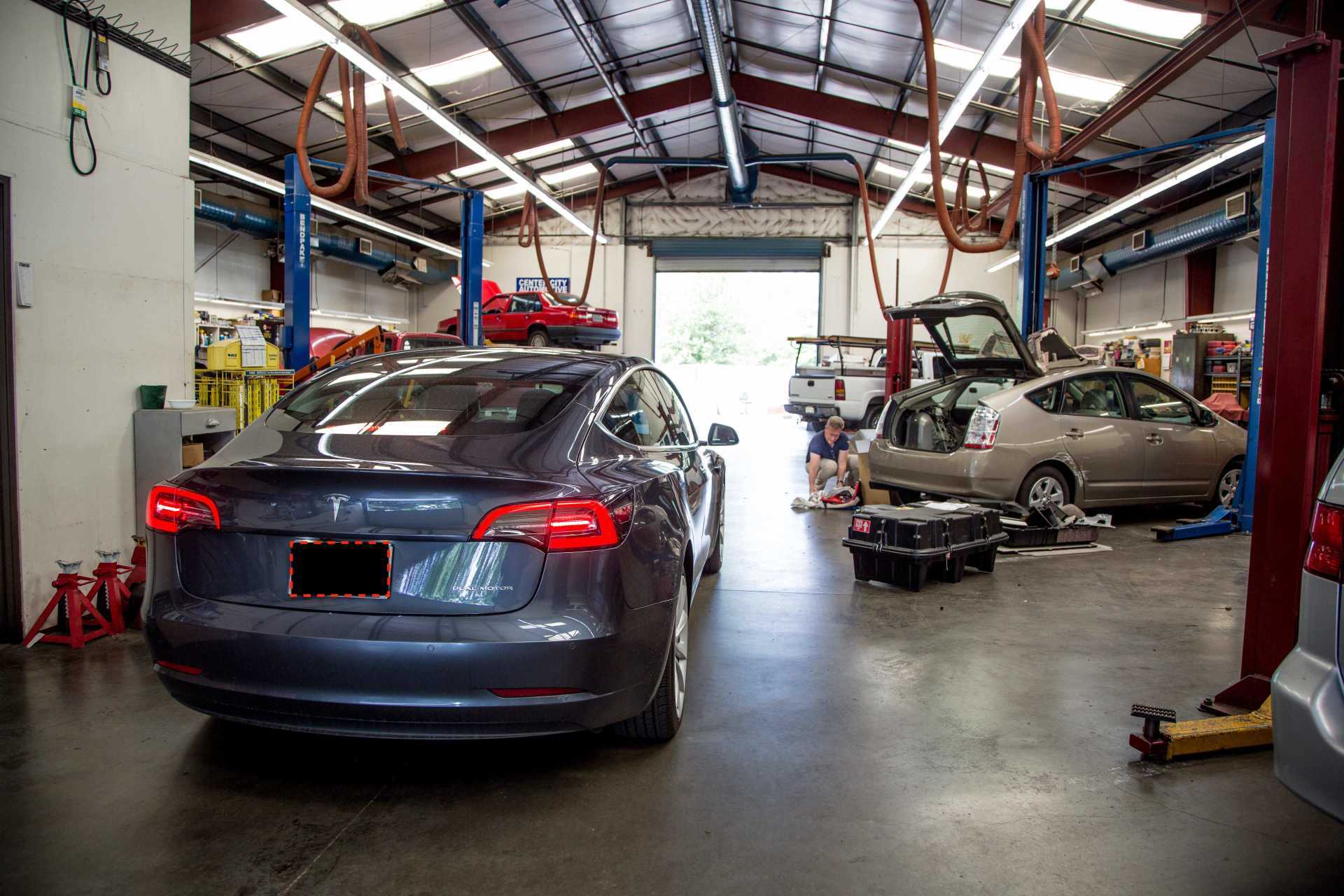 Auto repair shop with two cars, one dark sedan and one silver car being serviced on a lift.