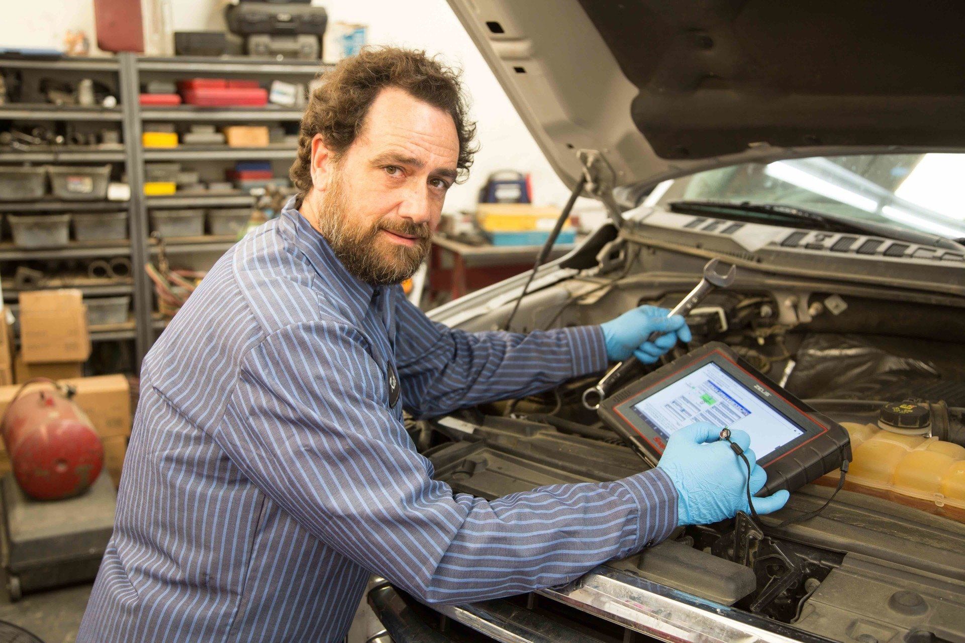 Mechanic in blue gloves using a tablet to diagnose a car with the hood open in a garage