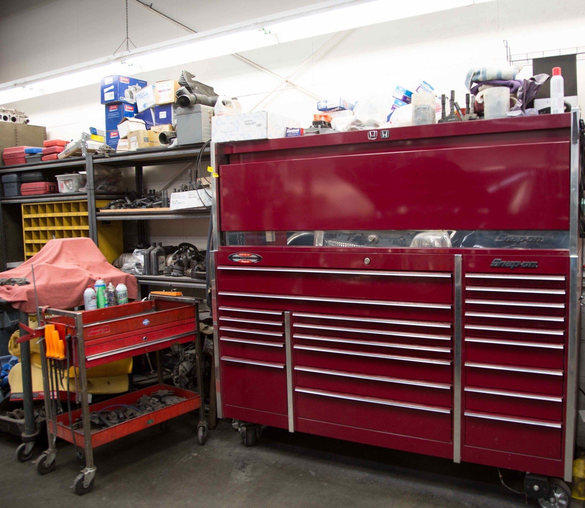 Red tool chest in a cluttered workshop beside metal shelves and stored supplies