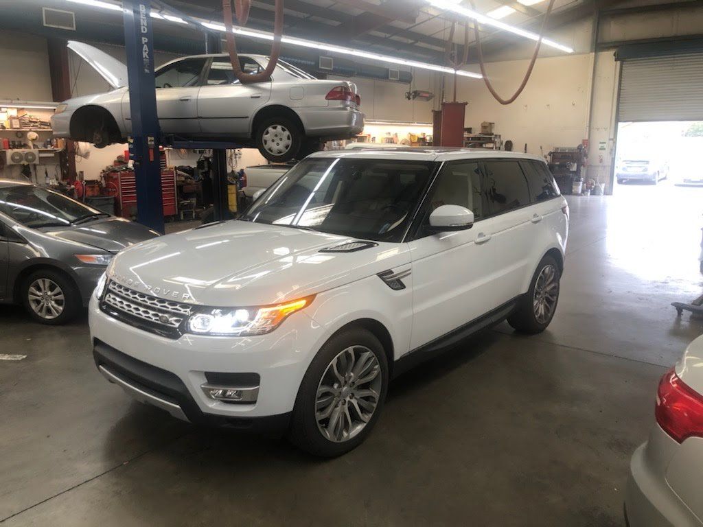 White SUV parked inside an auto repair shop with cars on lifts in the background