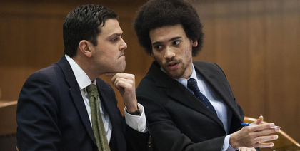 Two men in suits and ties are sitting next to each other in a courtroom.