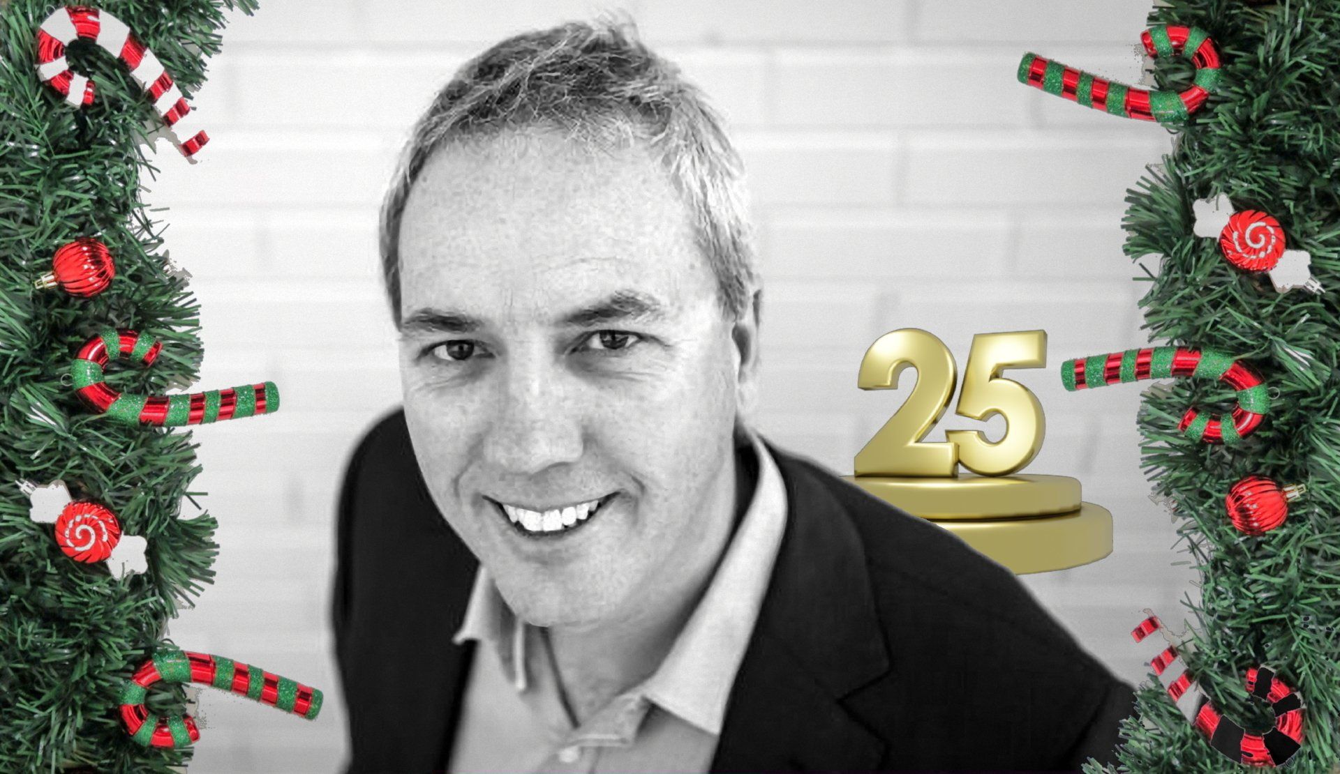 Man smiling, black and white. Surrounded by Christmas decorations, with 
