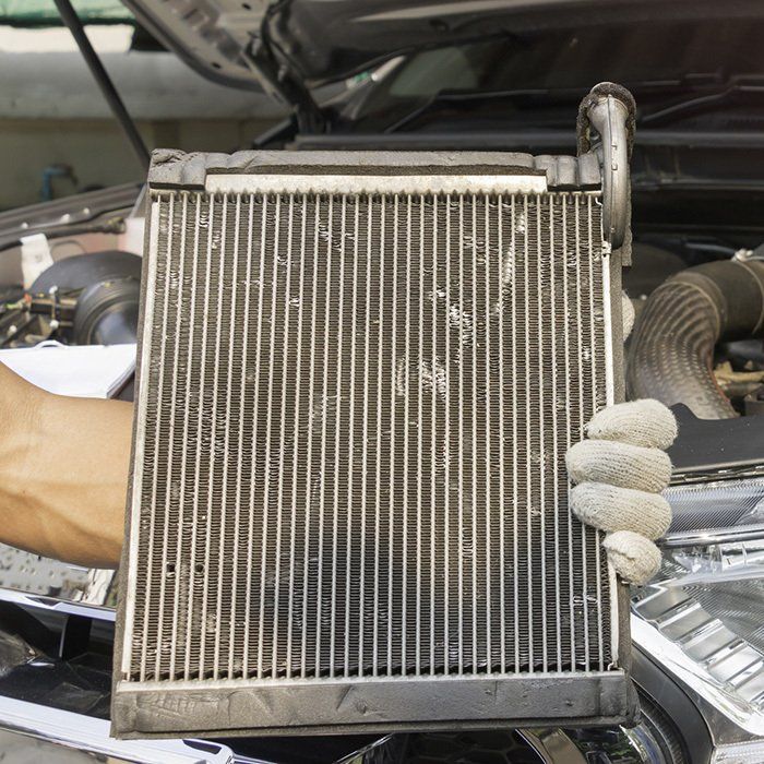 Hand holding a car heater core, likely for replacement, in an open engine bay.