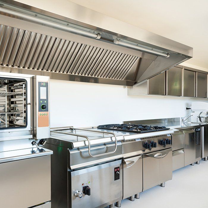 Commercial kitchen with stainless steel appliances: oven, range, hood, and cabinetry.