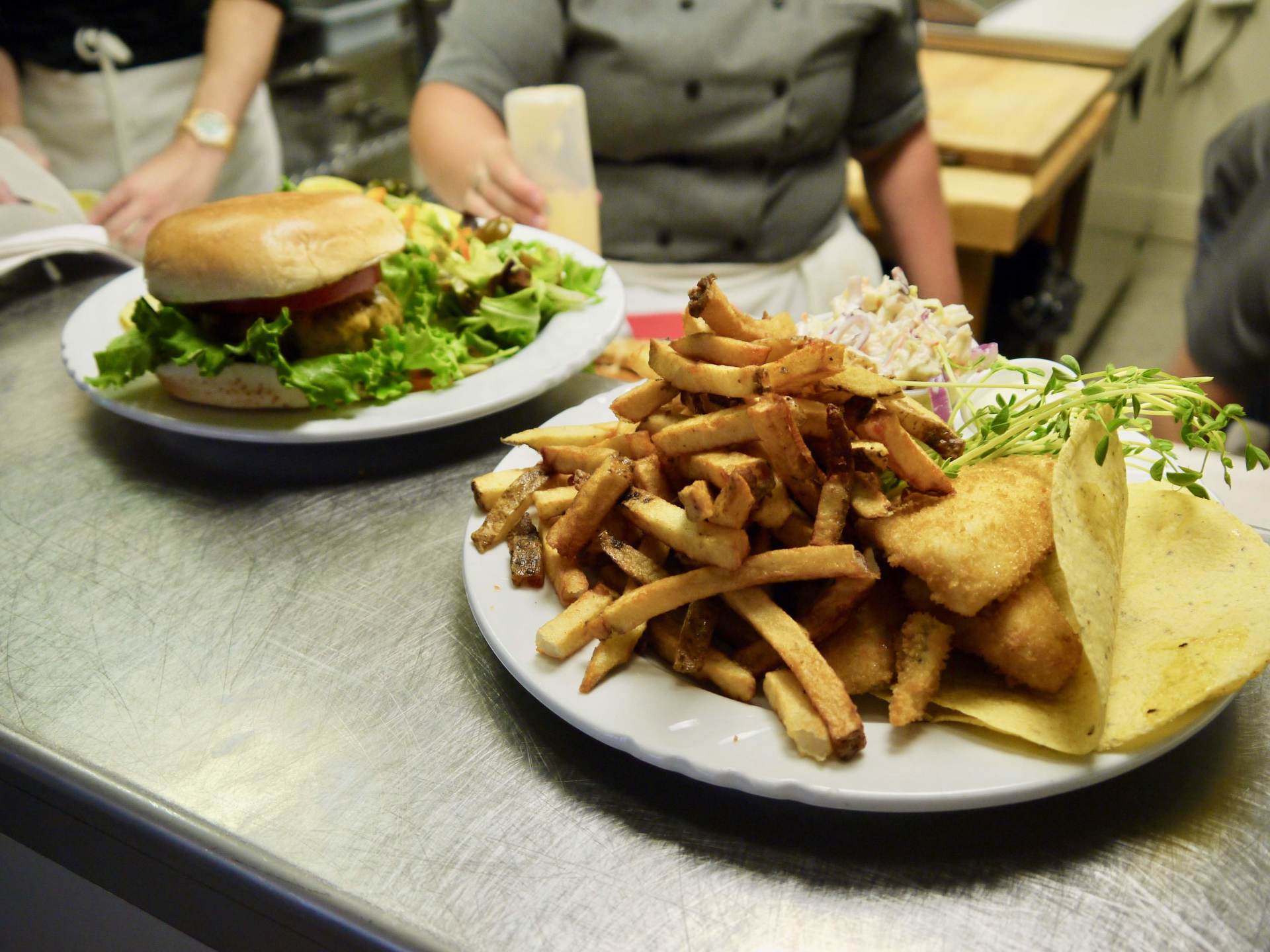 Two plates of food on a counter including a hamburger and french fries