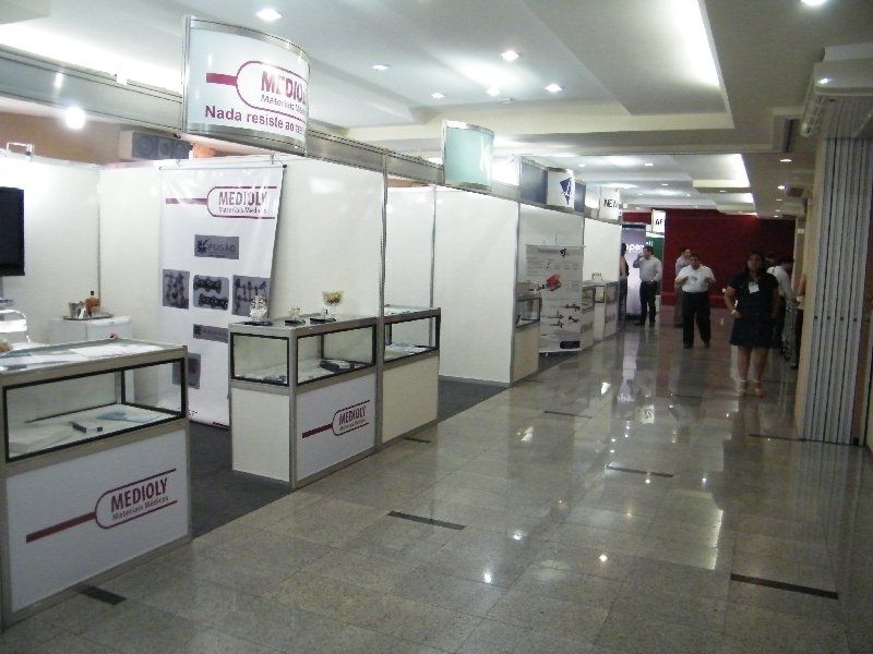 Corredor interno de shopping com barracas brancas de vendedores e algumas pessoas caminhando ao longe.