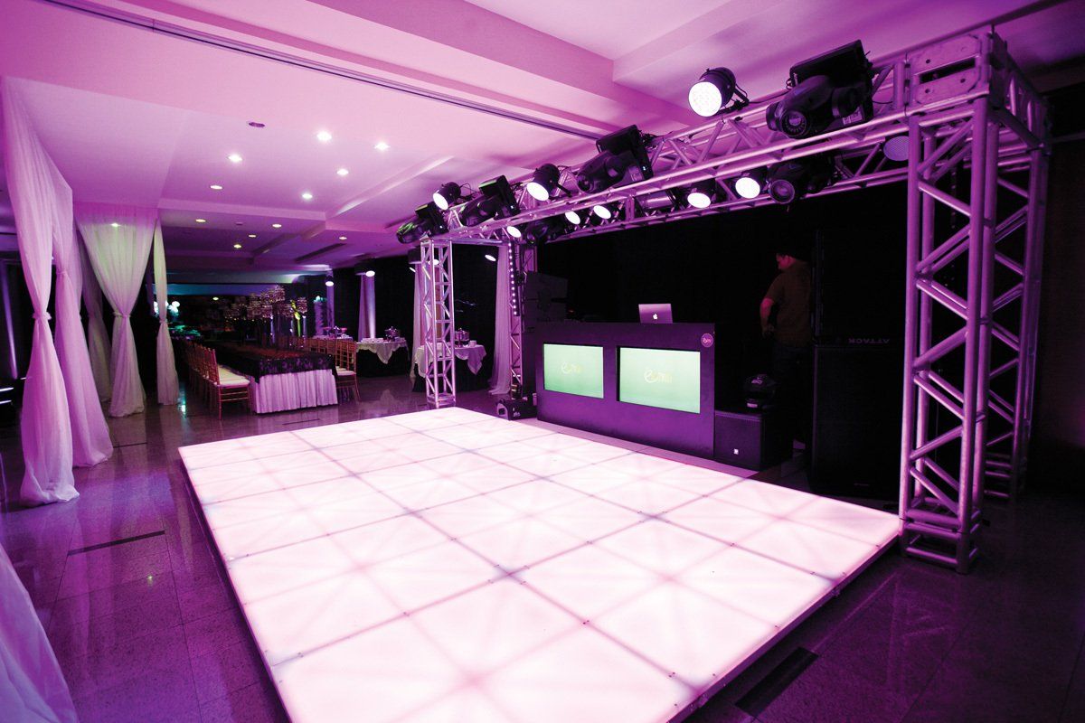 Espaço para eventos com iluminação roxa, pista de dança iluminada e estrutura de iluminação de palco.