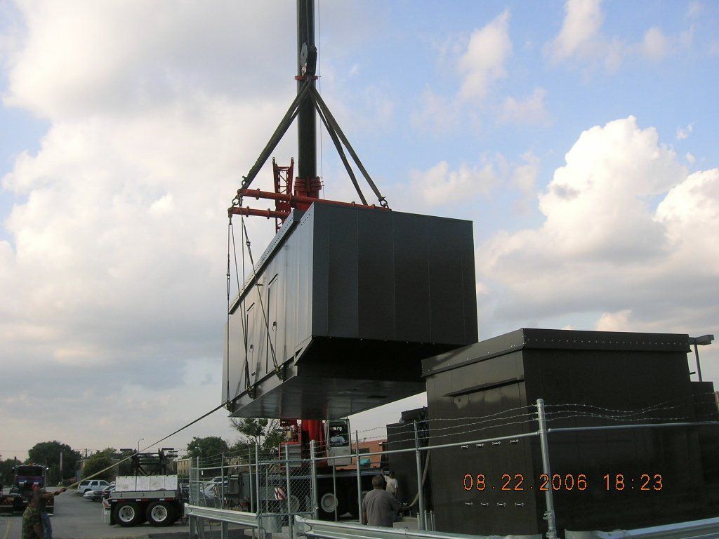A large black box is being lifted by a crane on a cloudy day