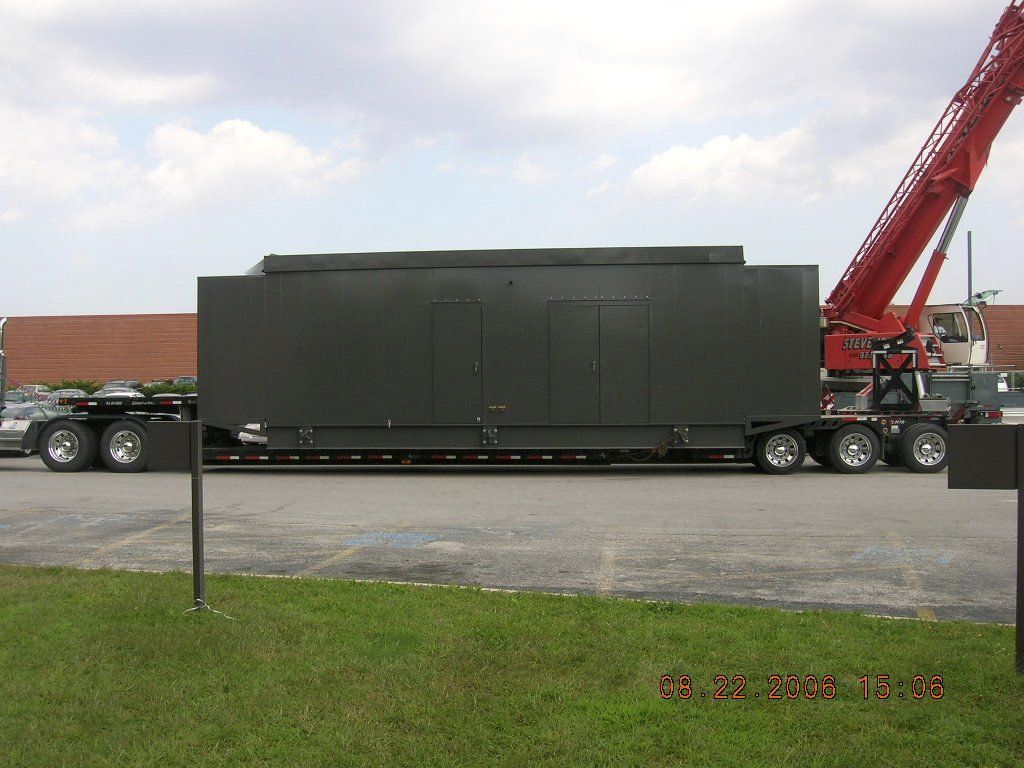 A red crane is lifting a large black box on a trailer