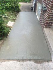 Freshly poured concrete walkway next to a red brick wall and greenery.