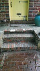 Brick steps leading to a yellow door on a brick building; a teal planter sits on the right.