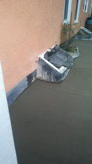 Freshly poured concrete patio against a salmon-colored building with a window well.