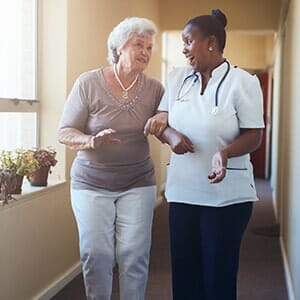 Happy healthcare worker walking and talking with senior woman - medical home in Elmhurst, NY Happy healthcare worker walking and talking with senior woman - medical home in Elmhurst, NY