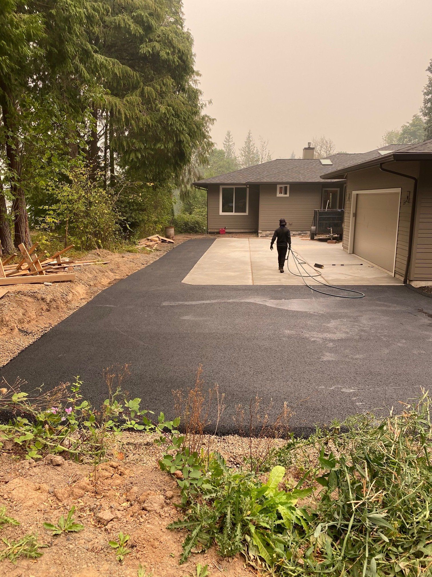 Asphalt driveway leads to a house; person walking towards the house, hazy sky.