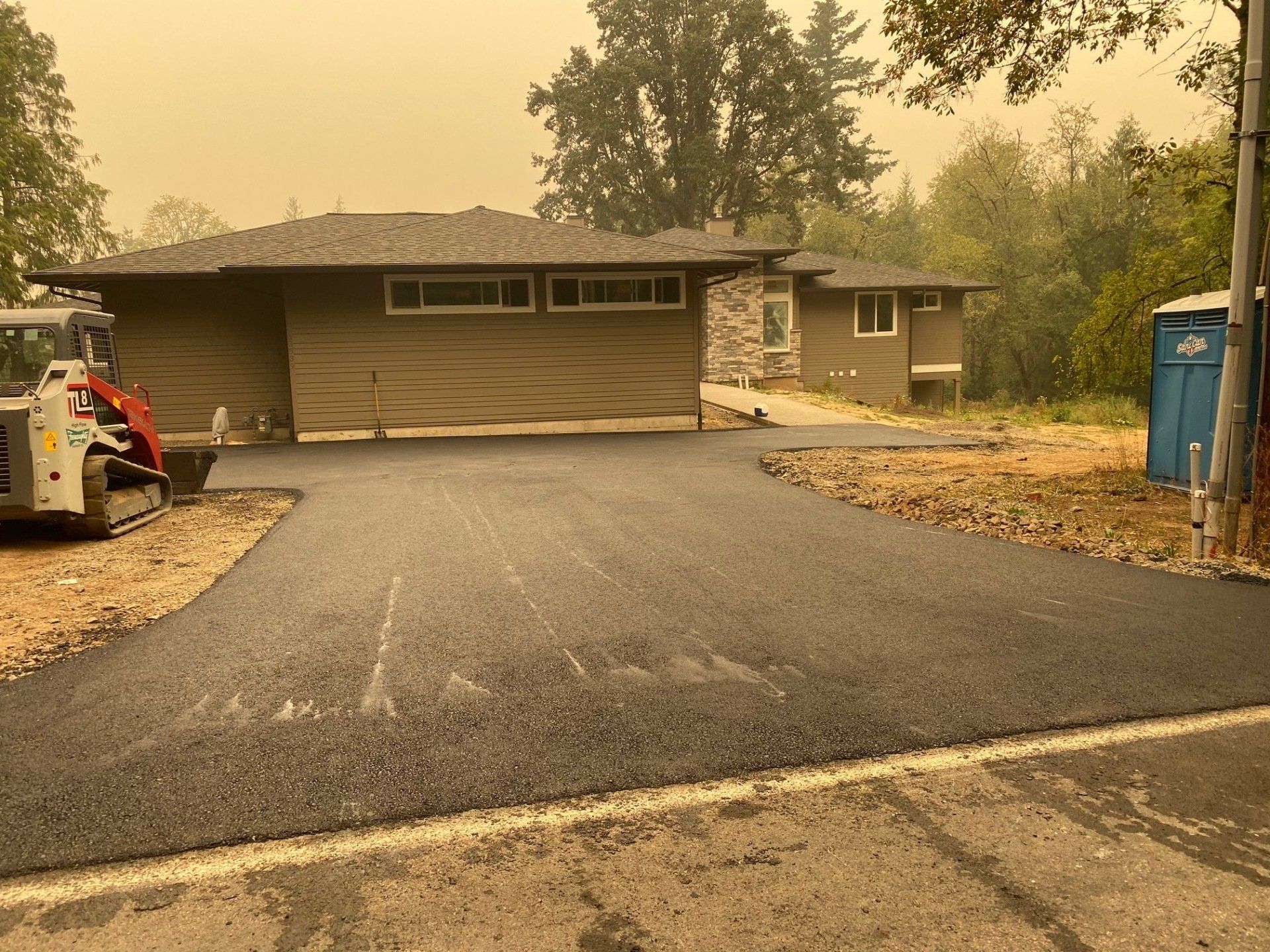 A newly paved asphalt driveway leads to a one-story house. A small construction vehicle sits on the left.