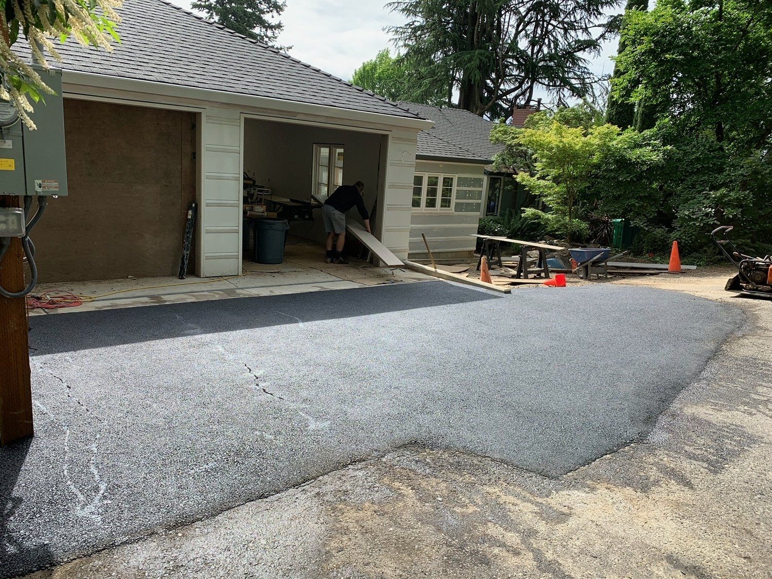 Asphalt driveway leading to a garage under construction; a worker inside.